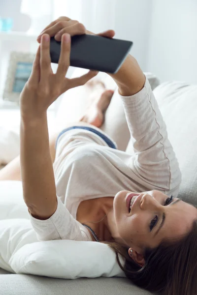 Mooie jonge vrouw met behulp van haar mobiele telefoon thuis. — Stockfoto