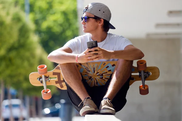 Knappe skater jongen met zijn mobiele telefoon in de straat. — Stockfoto