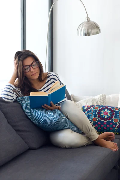 Vacker ung kvinna läser en bok på soffan. — Stockfoto