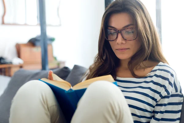 Piękna młoda kobieta czytająca książkę na sofie. — Zdjęcie stockowe