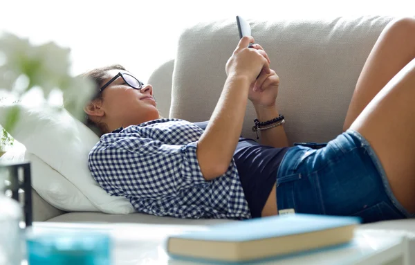 Mooie jonge vrouw met behulp van haar mobiele telefoon thuis. — Stockfoto