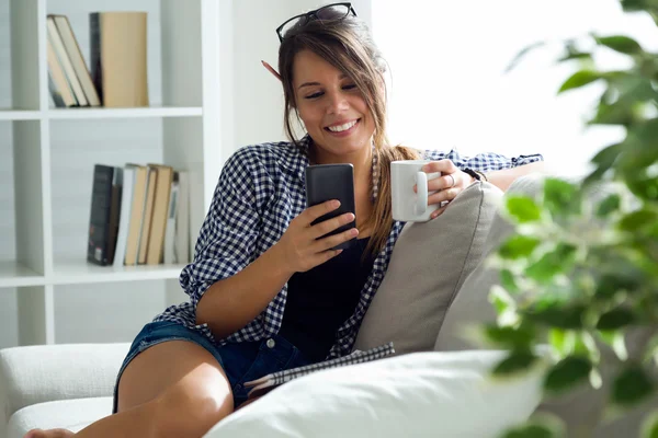 Mooie jonge vrouw met behulp van haar mobiele telefoon thuis. — Stockfoto