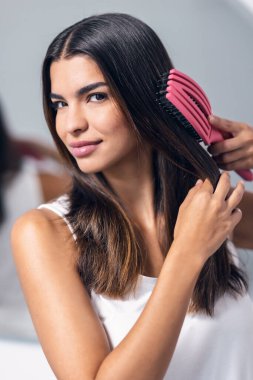 Banyoda aynanın önünde uzun saçlarını tarayan güzel bir genç kadının portresi.