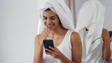 Banyoda dişlerini fırçalarken akıllı telefon kullanan güzel bir kadının videosu.