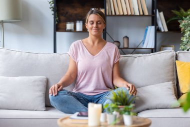 Evdeki kanepede yoga yapan rahatlatıcı bir kadın.