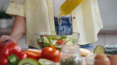 Genç bir kadının salatayı evdeki mutfakta yağla tatlandırdığı yakın çekim videosu..