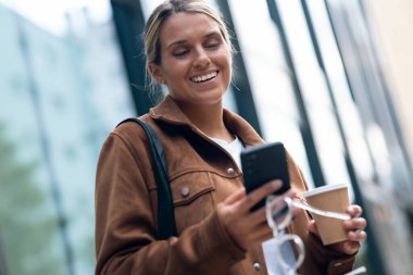 Şehirde kahve içerken akıllı telefonunu kullanan güzel bir kadının fotoğrafı.