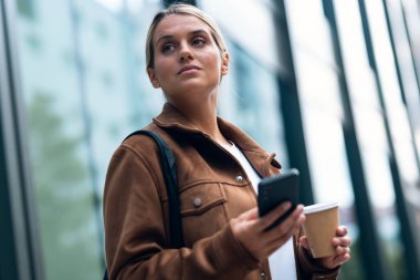 Şehirde kahve içerken akıllı telefonunu kullanan güzel bir kadının fotoğrafı.