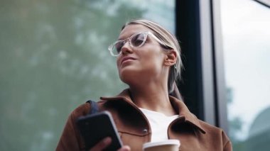 Şehirde kahve içerken akıllı telefonunu kullanan güzel bir kadının videosu.