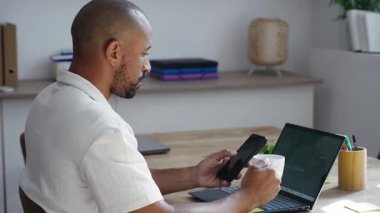 Ofiste telefonunu kullanırken bilgisayarında istatistiklerle çalışan iş adamının videosu.