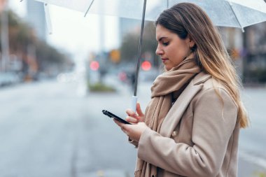 Yağmurda şemsiyeyle yürürken güzel bir kadının telefonunu kullanması.