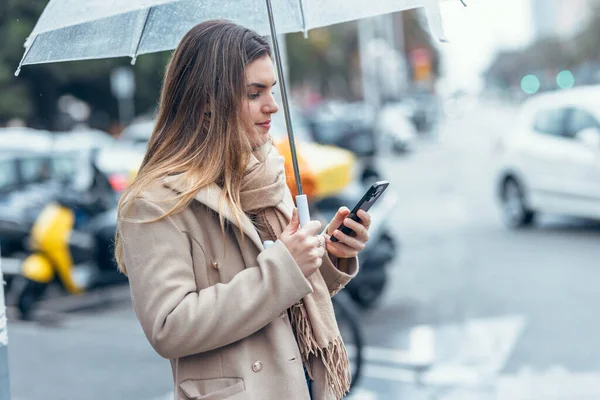 Yağmurda şemsiyeyle yürürken güzel bir kadının telefonunu kullanması.