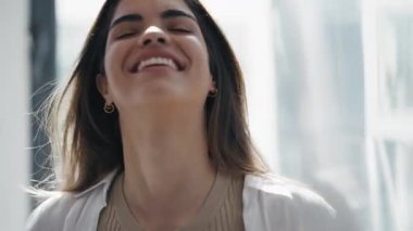 Evdeki oturma odasında kameraya bakarken gülümseyen genç bir kadının görüntüsü..