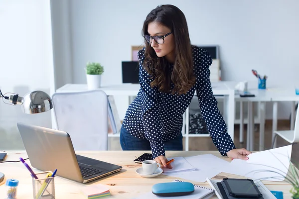 Frumos femeie tânără care lucrează cu laptop în biroul ei . — Fotografie, imagine de stoc