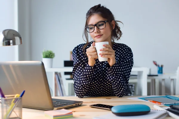 Schöne junge Frau trinkt Kaffee in ihrem Büro. — Stockfoto