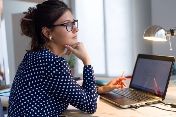 Mooie jonge vrouw met laptop in haar kantoor werken. — Stockfoto