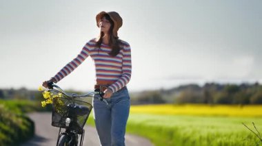 Bisikletin yanında yürüyen genç ve güzel bir kadının baharın çiçeklerinin tadını çıkardığı bir video..