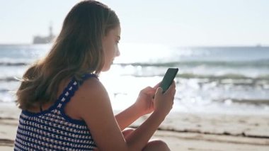 Deniz kenarında otururken akıllı telefon kullanan tatlı bir kızın videosu.
