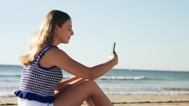 Deniz kenarında otururken akıllı telefonuyla selfie çeken tatlı bir kızın videosu.