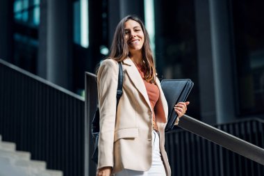 Sokakta poz verirken ve kameraya bakarken elinde dizüstü bilgisayarla gülümseyen genç bir iş kadını..