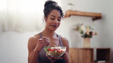 Evde kulaklıkla müzik dinlerken sağlıklı meyve kasesi yiyen atletik bir kadının videosu.