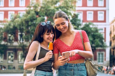 İki gülümseyen kadının şehirde gezerken akıllı telefon kullanması.