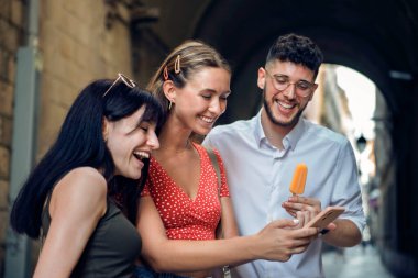 Şehri gezerken telefonlarını kullanan üç mutlu arkadaştan oluşan bir grup.