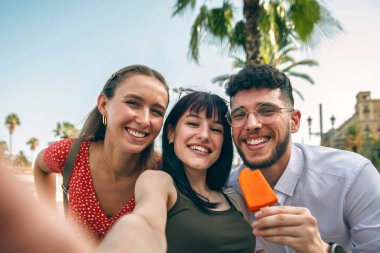 Üç mutlu arkadaştan oluşan bir grup akıllı telefonla şehri gezerken selfie çekiyor.