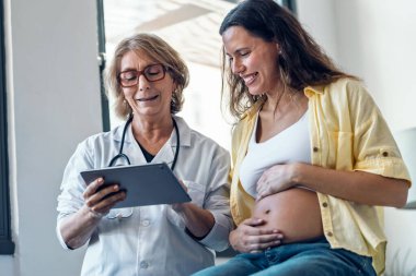 Kadın jinekolog hamile bir kadına ultrason görüntüsü veriyor. Bebek dijital tabletle tıbbi konsültasyonda.