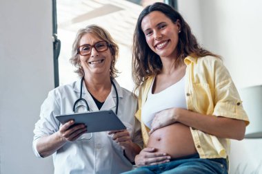 Kadın jinekolog hamile bir kadına ultrason görüntüsü veriyor. Bebek dijital tabletle tıbbi konsültasyonda.