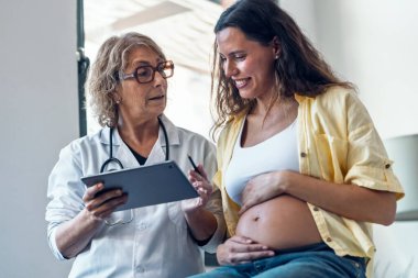 Kadın jinekolog hamile bir kadına ultrason görüntüsü veriyor. Bebek dijital tabletle tıbbi konsültasyonda.