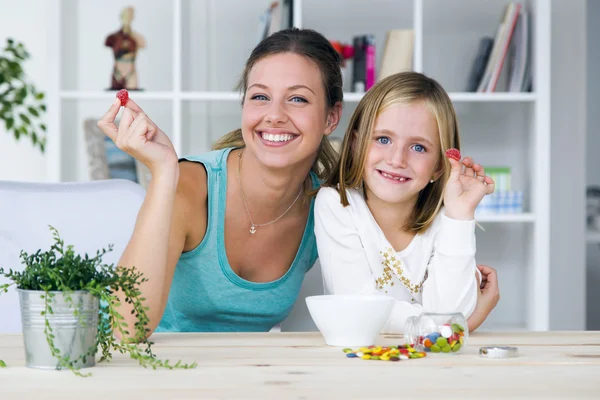 Jeune mère et fille mangeant des bonbons à la maison . — Photo