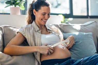 Hamile bir kadının, karnına kulaklık takıp evde kanepede otururken müzik dinleyebilmesi için.