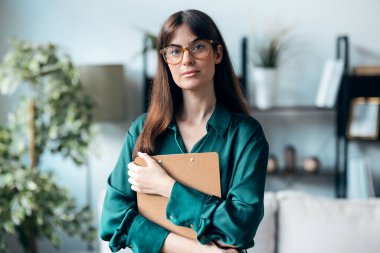 Ofisinde kameranın önünde poz verirken elinde bir klasör tutan kadın psikolog fotoğrafı.