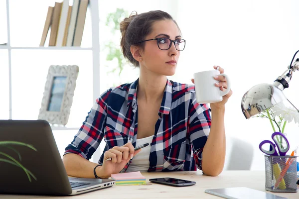 Vacker ung kvinna dricker kaffe i hennes kontor. — Stockfoto