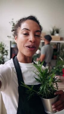 Güzel bayan çiçekçinin, bir çiçekçide iş arkadaşıyla çalışırken akıllı telefonuyla sosyal medya için video çektiği video.