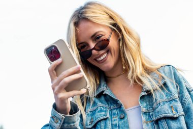 Şehirde yürürken akıllı telefonunu kullanan gülümseyen bir kadın.