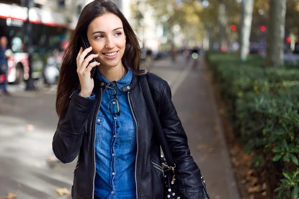 Vacker ung kvinna med hennes mobiltelefon på gatan. Stockbild