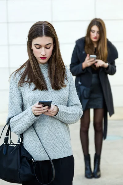 Twee jonge zakenvrouw met behulp van mobiele telefoon in de straat. — Stockfoto