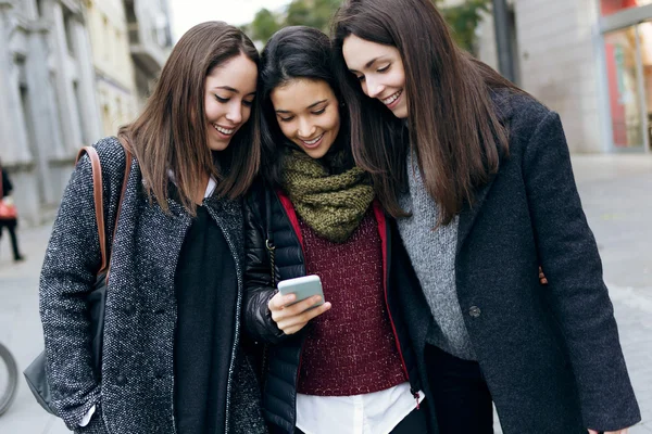 Retrato de tres mujeres hermosas jóvenes usando teléfono móvil . — Foto de Stock