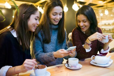 Üç genç güzel kadın cep telefonuyla kafe dükkanında.