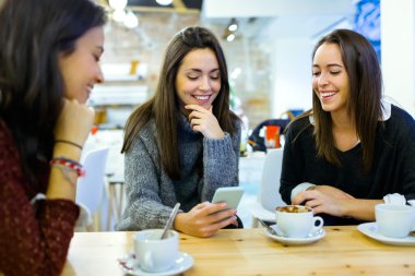 Üç genç güzel kadın cep telefonuyla kafe dükkanında.