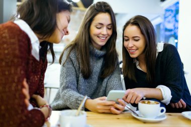 Üç genç güzel kadın cep telefonuyla kafe dükkanında.