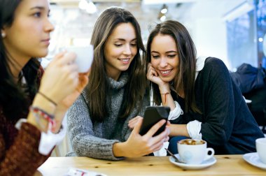 Üç genç güzel kadın cep telefonuyla kafe dükkanında.