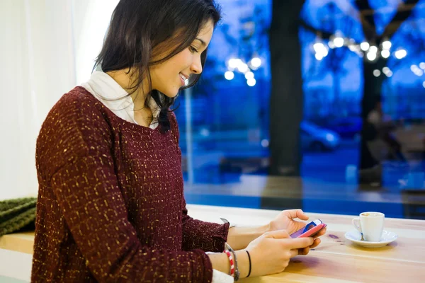 Mooie jonge vrouw met behulp van haar mobiele telefoon bij café shop. — Stockfoto