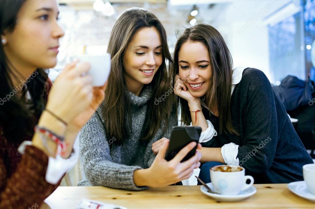 Three young beautiful women using mobile phone at cafe shop.