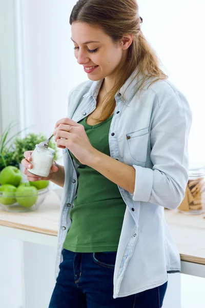 Mujer bastante joven comiendo yogur en la cocina . — Foto de Stock
