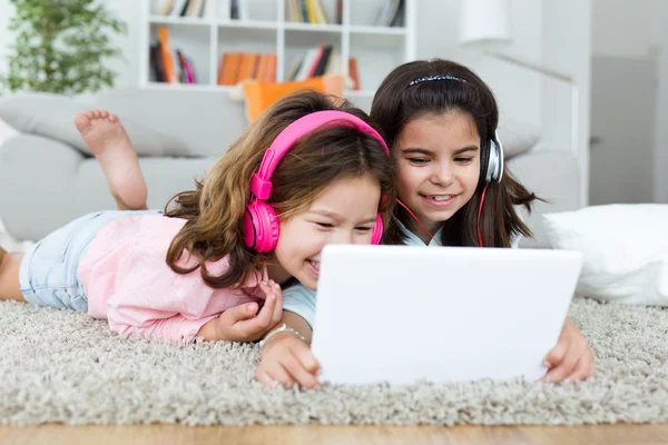 Mooie jonge zussen luisteren naar muziek met digitale tablet. — Stockfoto