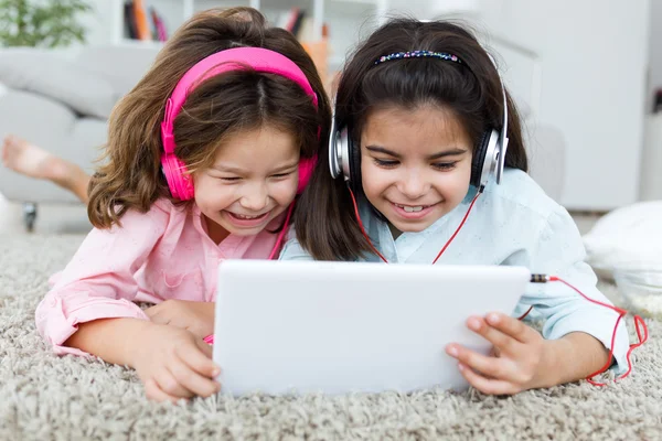 Mooie jonge zussen luisteren naar muziek met digitale tablet. — Stockfoto
