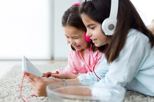 Vackra unga systrar lyssnar på musik med digital tablet. — Stockfoto